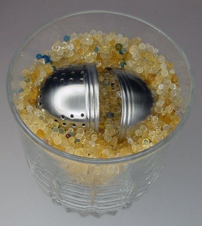 Submerging a stainless steel tea ball into a container of silica gel beads to completely fill the inside of the tea ball.
