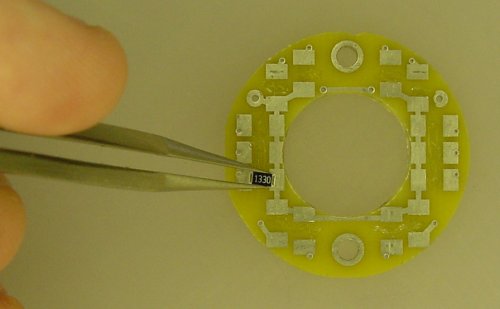 Placing surface-mount resistors on a printed circuit board using tweezers. Although it is hard to tell, I was able to get silicone in place for all fourteen parts.