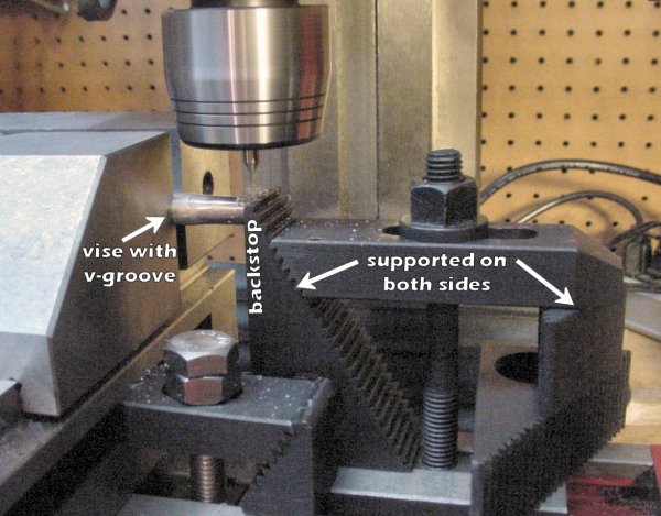 A milling vise with a v-groove holds a rod on the milling machine. A workpiece stop made from a clamping set (step blocks, a holddown bar, stud, tee nut, and flange nut).