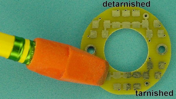 Erasing tarnish from a circuit board with a classic red pencil cap eraser.