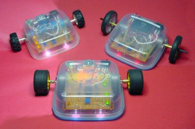 Three robots: Blue Sandwich (top left) with a printed circuit board; Red Sandwich (top right) with phototransistors, taller wheels, and a 6-volt battery pack; and the original Sandwich (bottom center) with point-to-point wiring and no headlight brightness adjustment